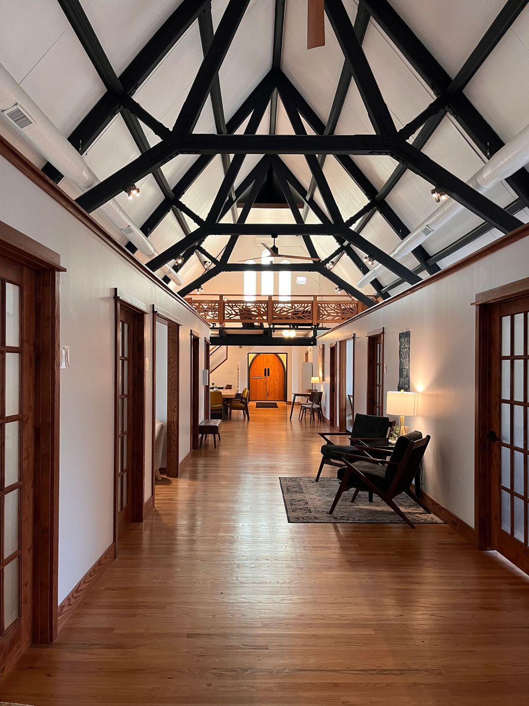 Hallway with wooden floors, white walls, black rafters, and brown doors.