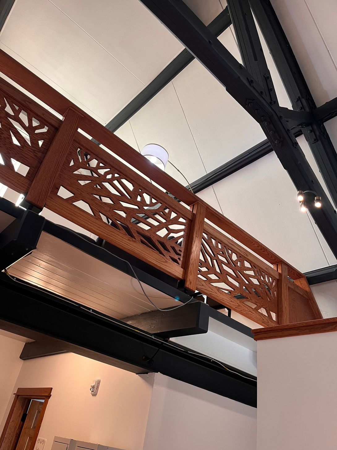 Decorative wooden railing with a nature-inspired design spans a room with dark beams and a white ceiling.