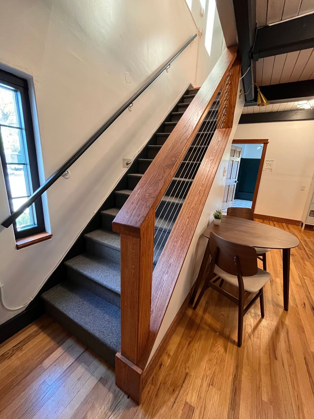 Staircase with wooden railing and carpeted steps, leading up. Small round table and chair visible at base.