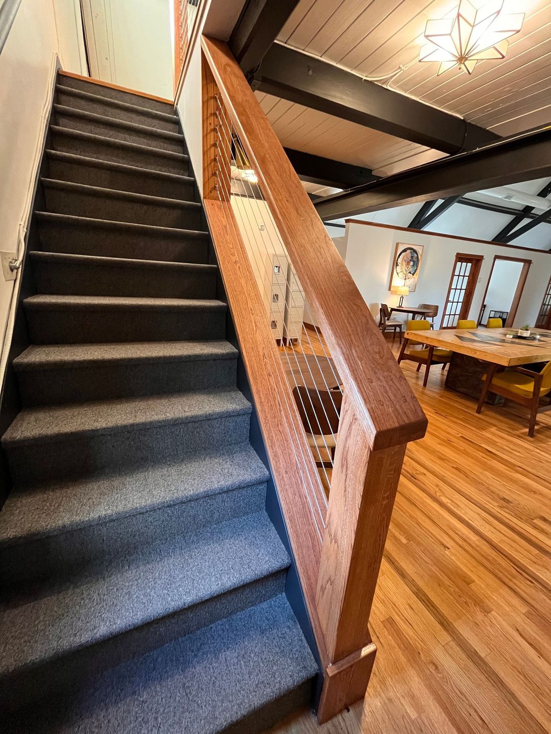 Staircase with carpeted steps and wooden railing. Brown railing runs alongside the stairs.