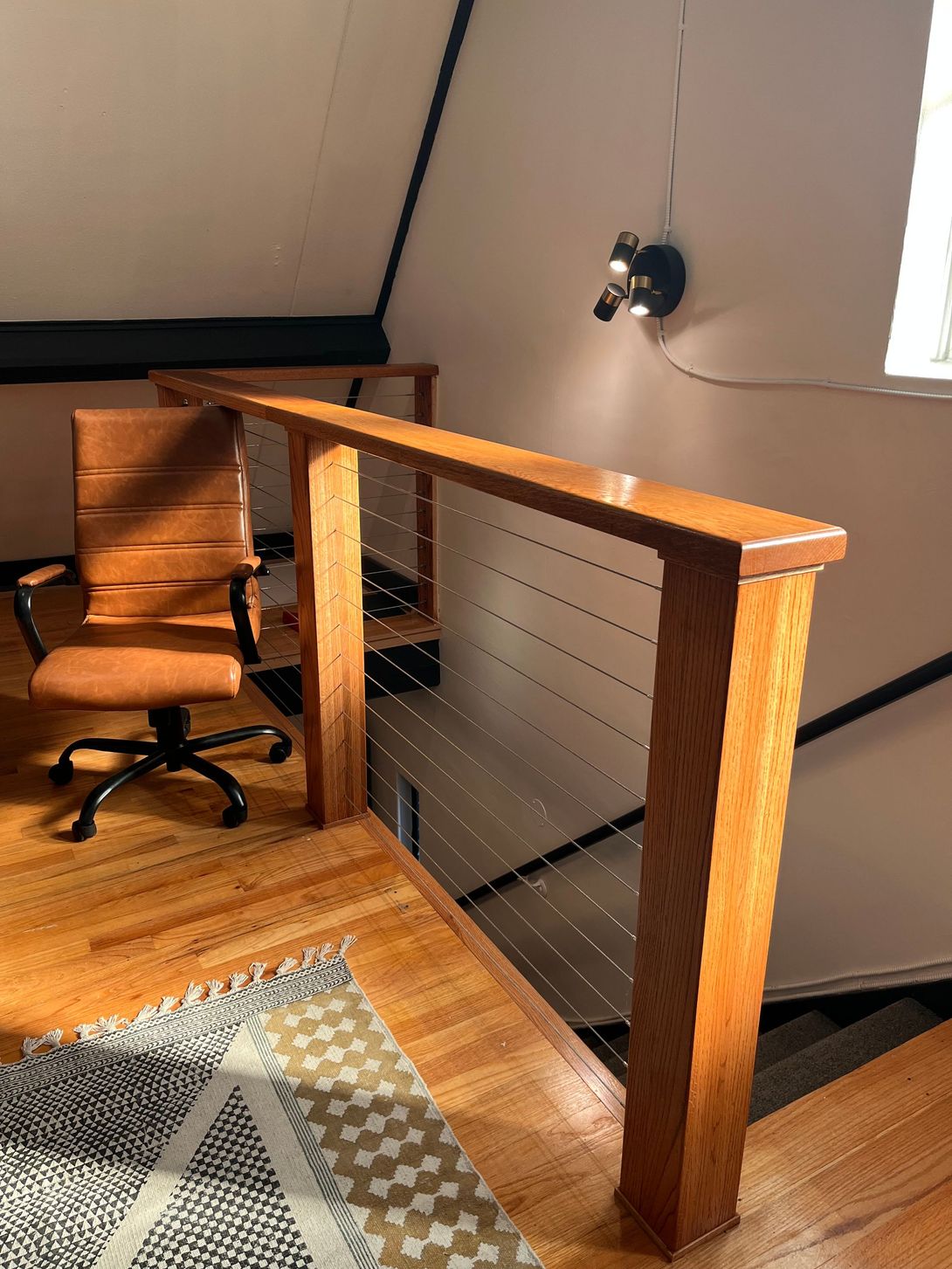 Wooden railing with cable infill in an attic workspace with a desk chair.