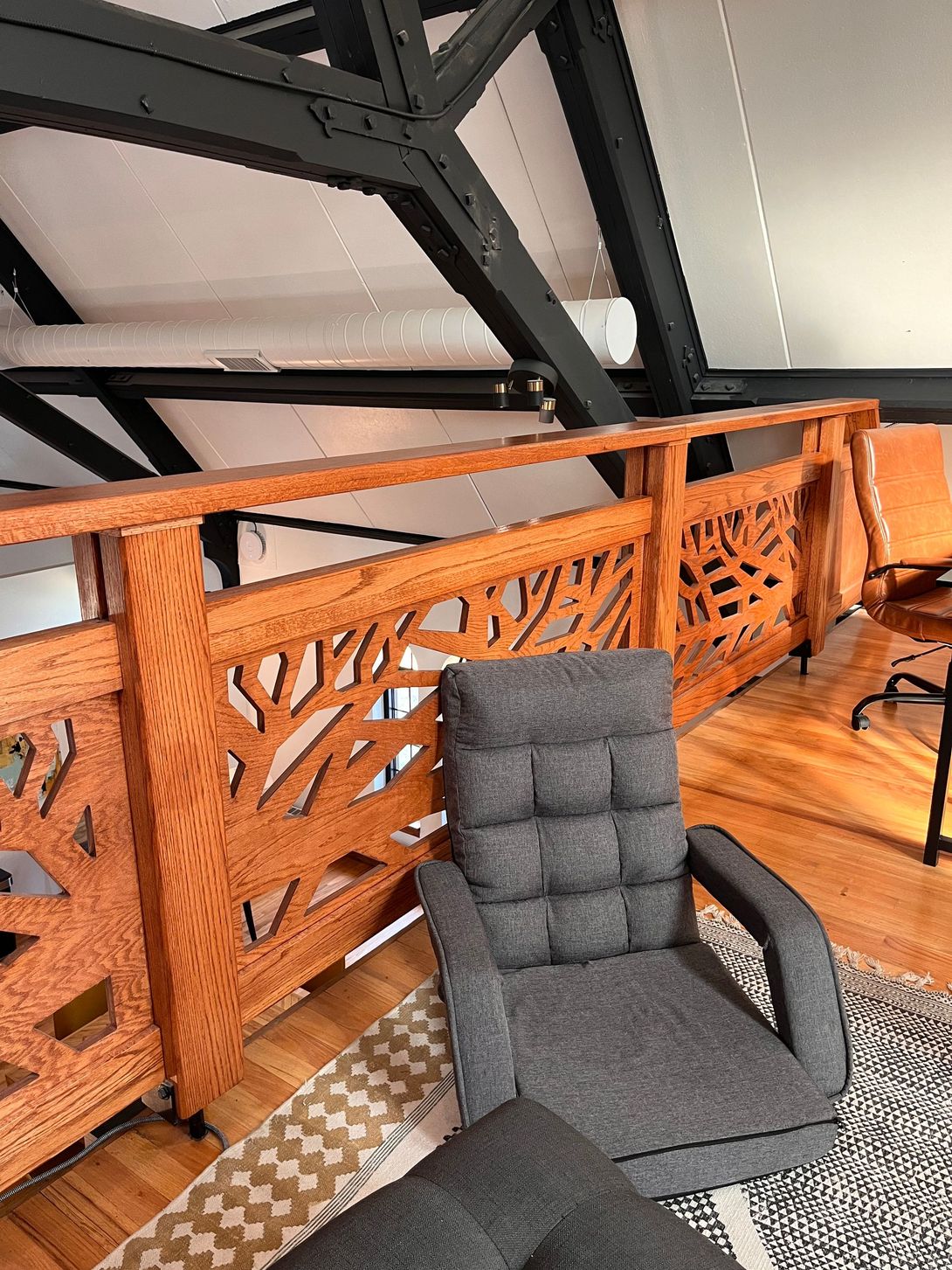 A cozy reading nook with a grey armchair, patterned rug, and wooden railing with a tree-like design.