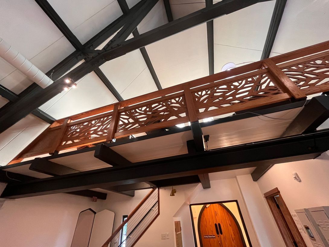 Loft with wood railing, open ceiling, and dark beams. Staircase and artwork in the foreground.