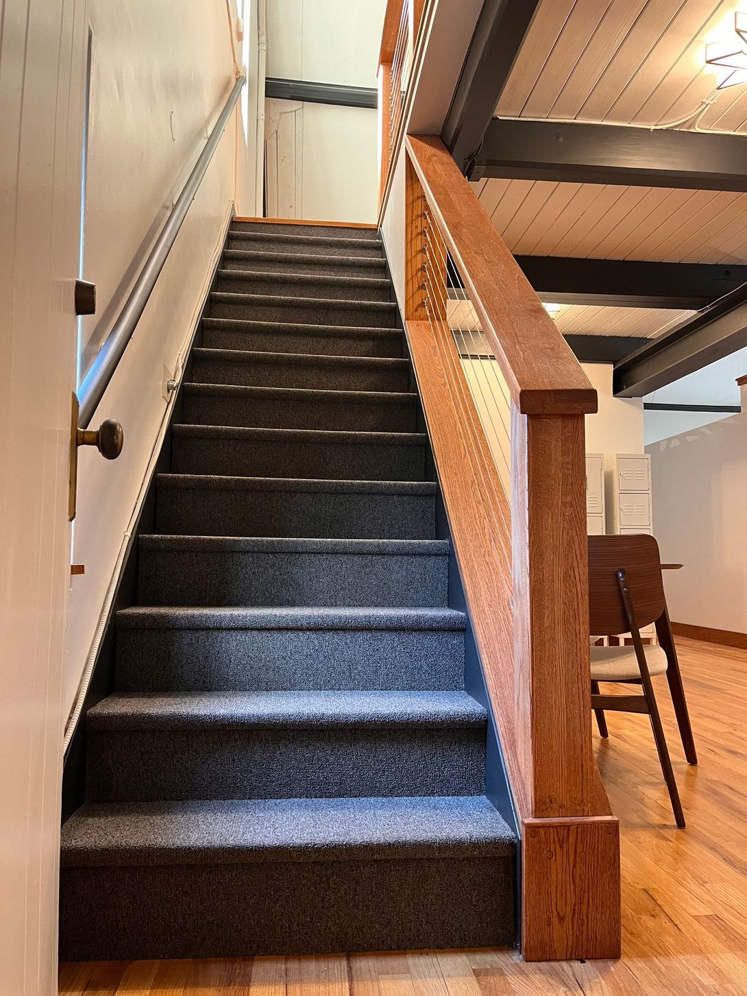 Staircase with carpeted steps, wooden railing, and dark ceiling beams. Interior shot.