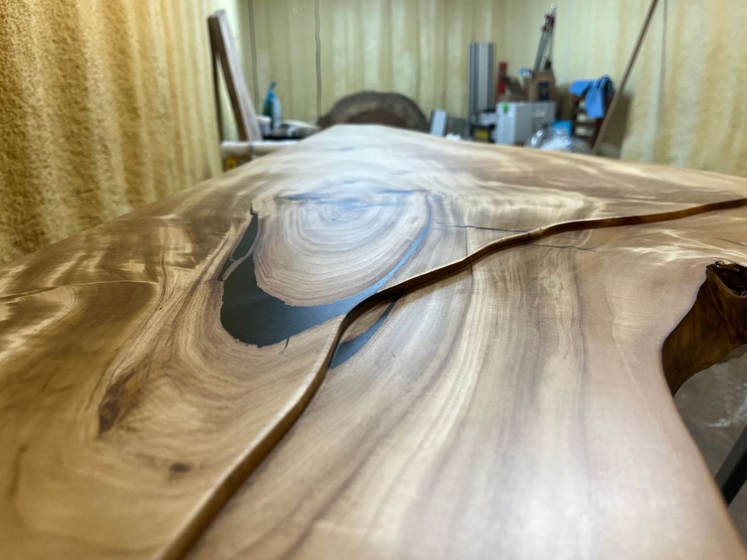 Close-up of a wooden table with a dark epoxy river. The wood is light brown, showing the grain.