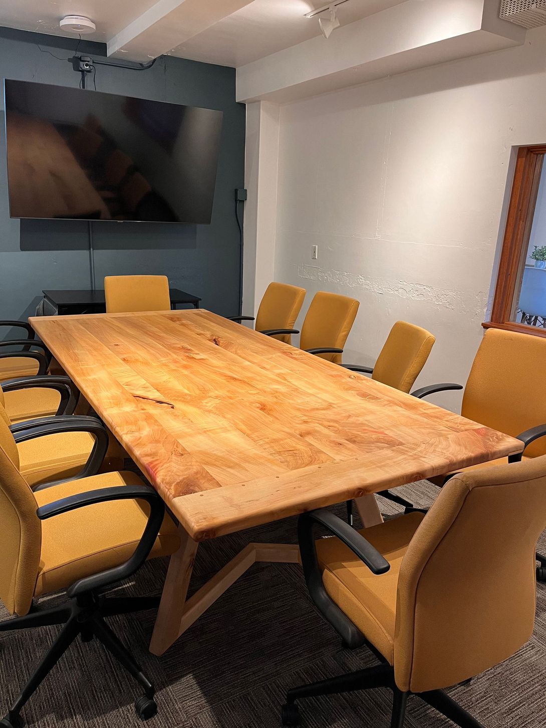 Conference room with large wooden table, yellow chairs, and a mounted television.