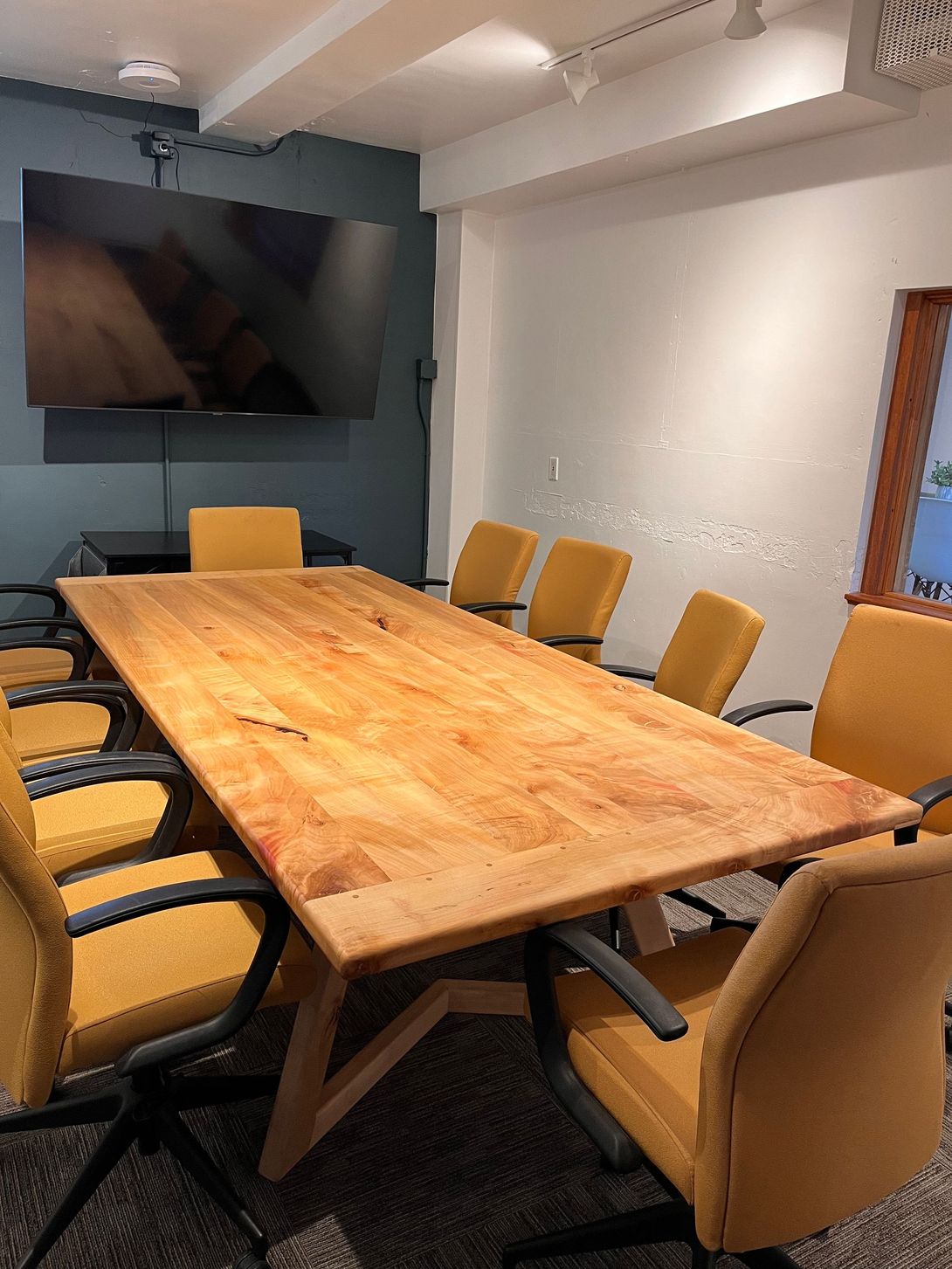 Meeting room with a wooden table, yellow chairs, and a large TV.