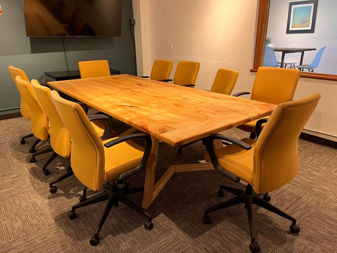 Meeting room with a large wooden table, yellow chairs, and a mounted TV.