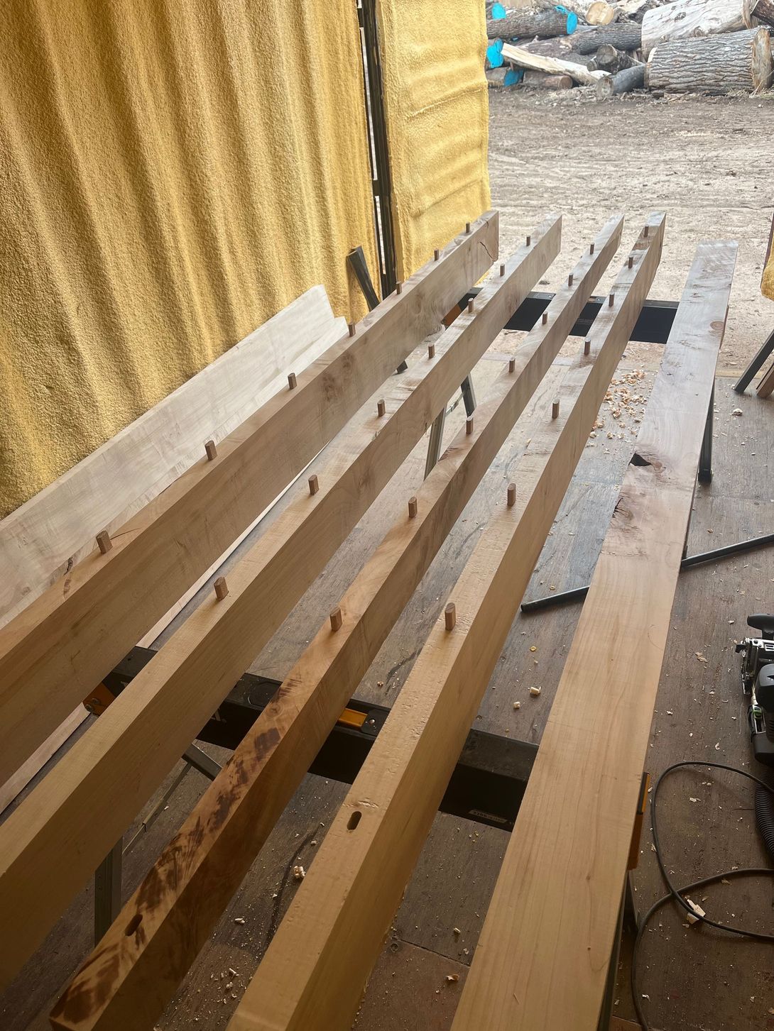 Wooden beams with dowels are laid out on a table in a workshop setting.