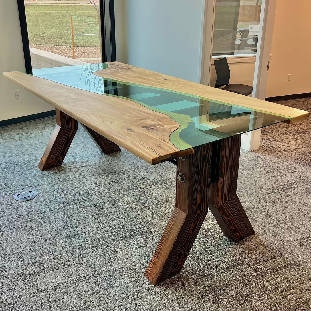 Wooden table with blue epoxy river, in a bright room with window.