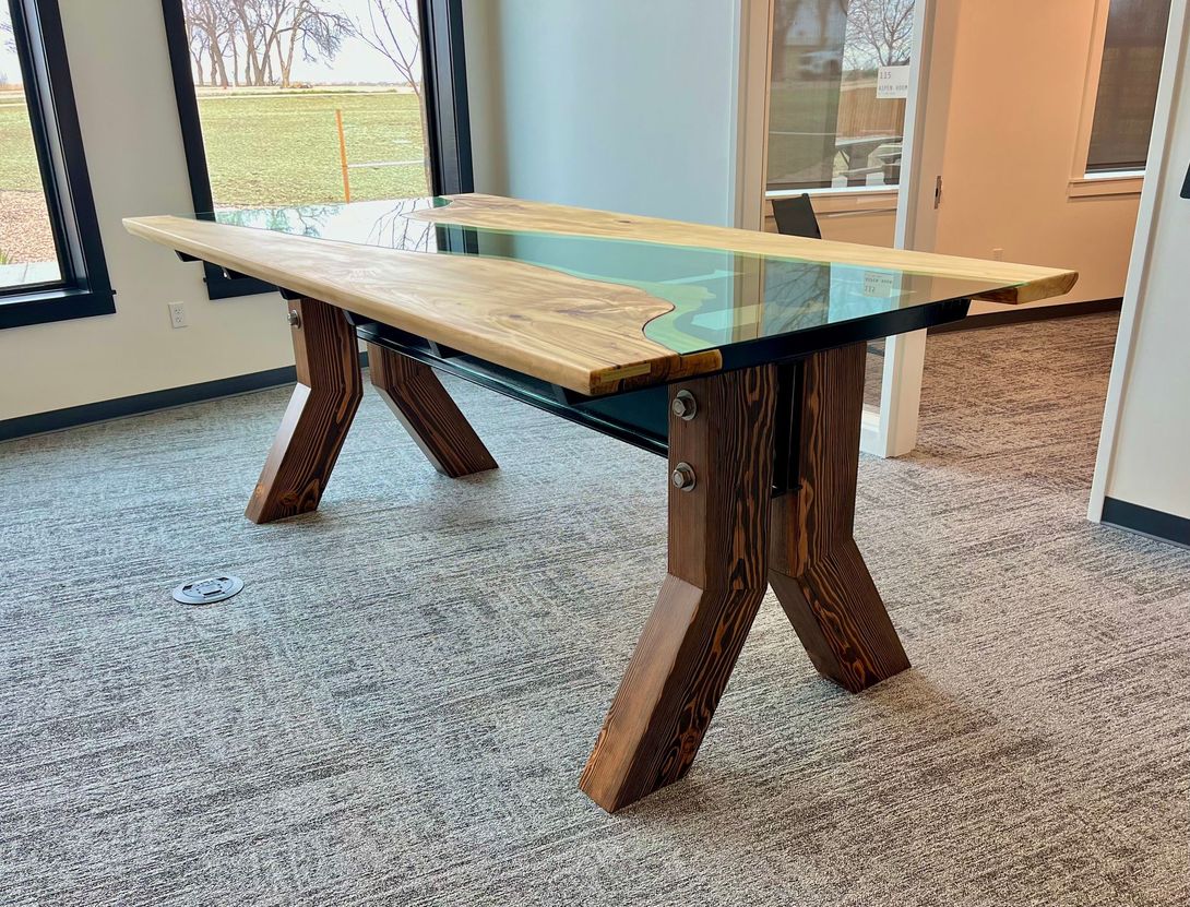 Wooden table with blue resin river running through it, set on a patterned carpet in a room.