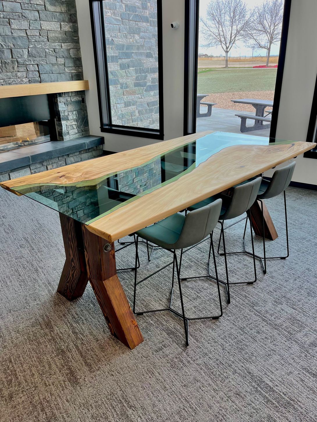 Live edge wood table with blue resin, four grey bar stools, and stone fireplace.