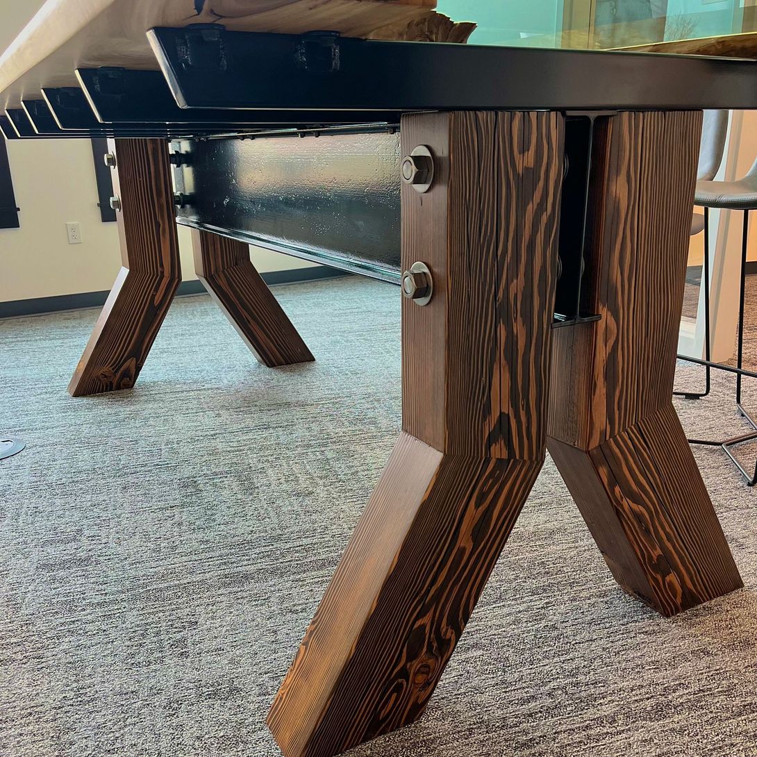 Wooden table with dark stained legs, bolted to black metal support beams.