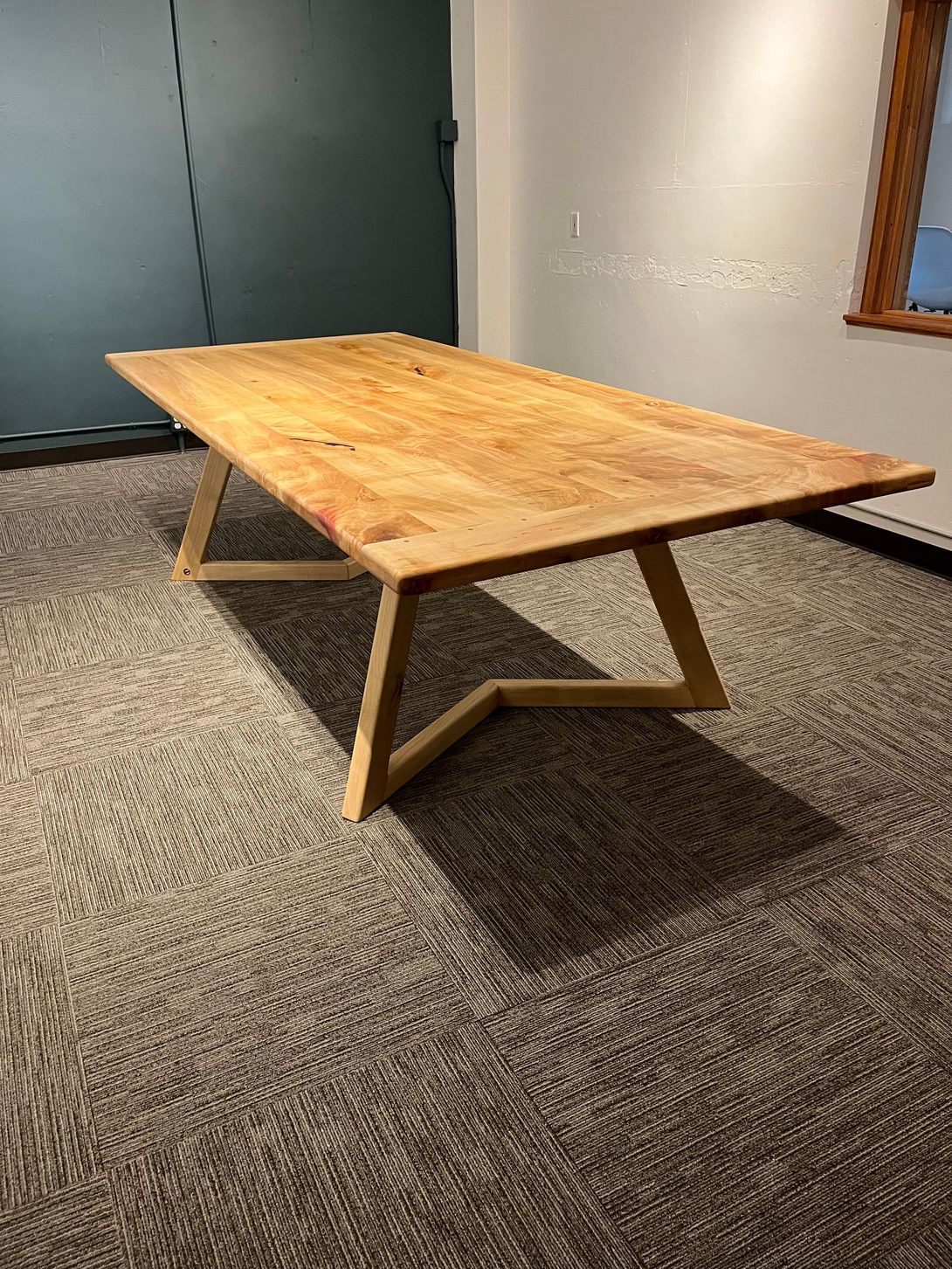 Wooden table with angled legs on patterned carpet.