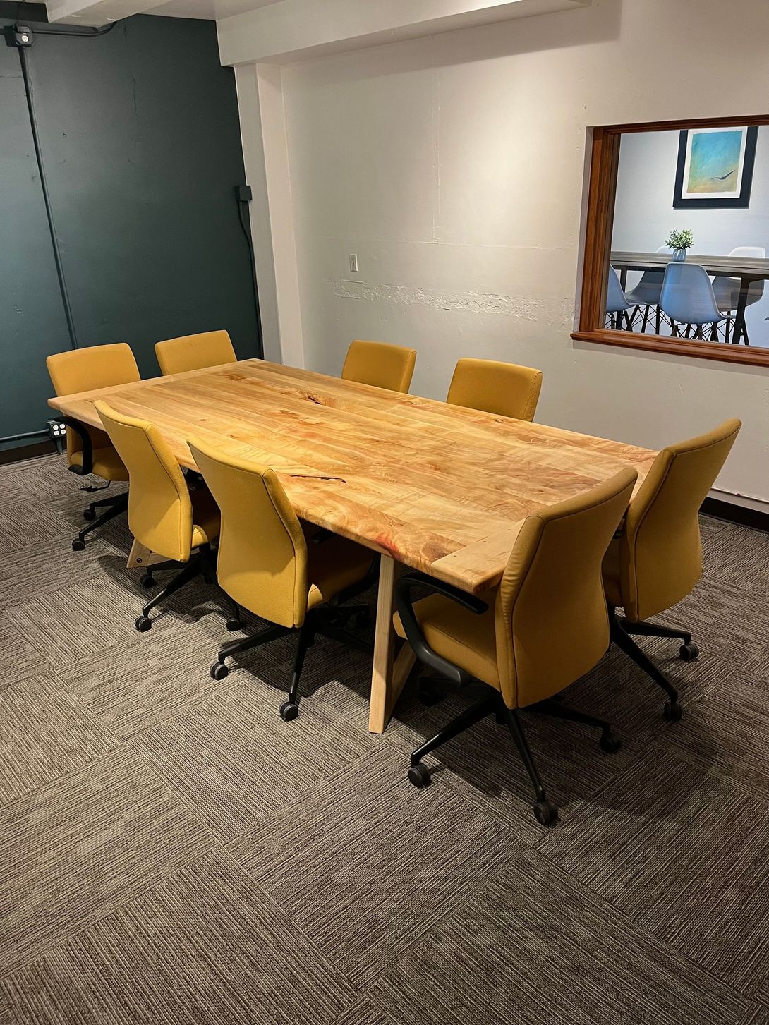 Conference room with large wood table, eight yellow chairs, and a peek-through window.