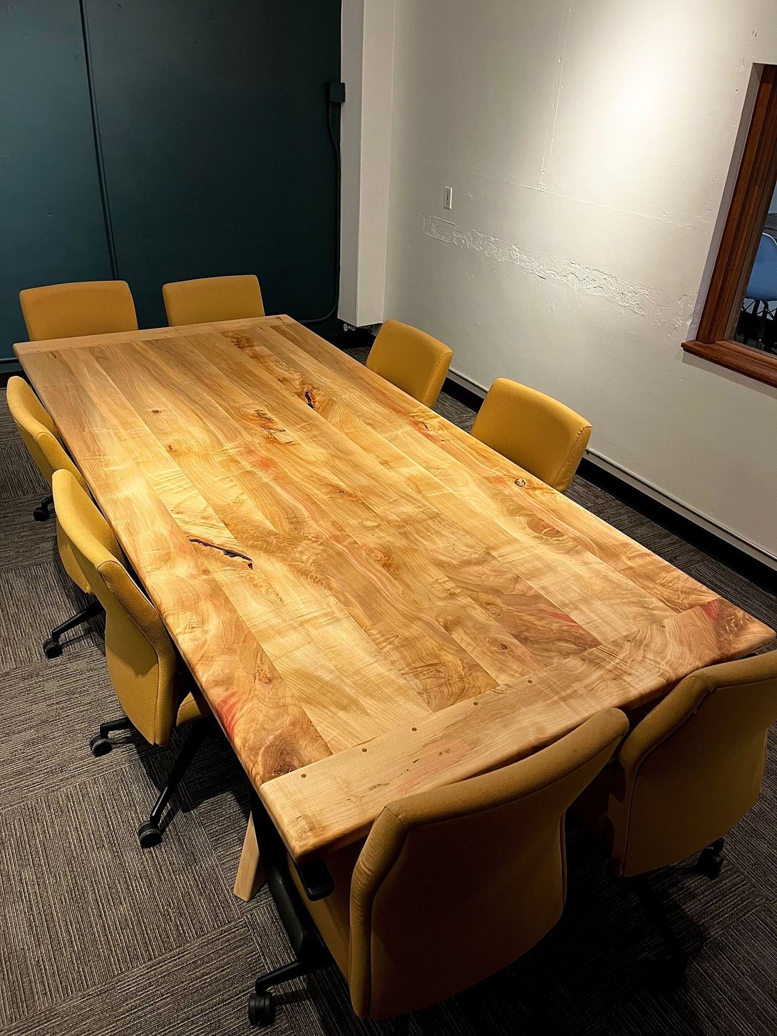 Large wooden conference table surrounded by eight yellow chairs in a room with dark green and light walls.