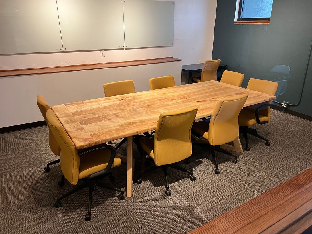 Conference room with wooden table, yellow chairs, whiteboard, and gray carpet.