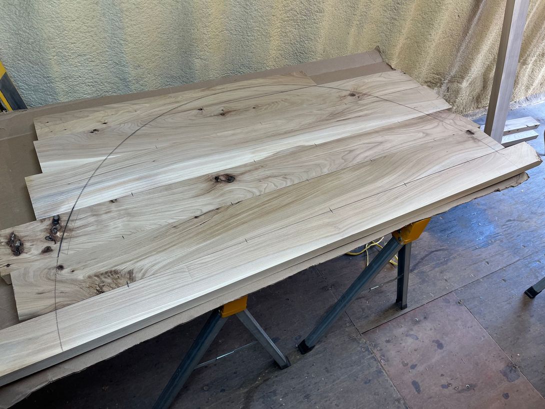 Wooden boards on a sawhorse, with a curved line drawn on one. Workshop setting.