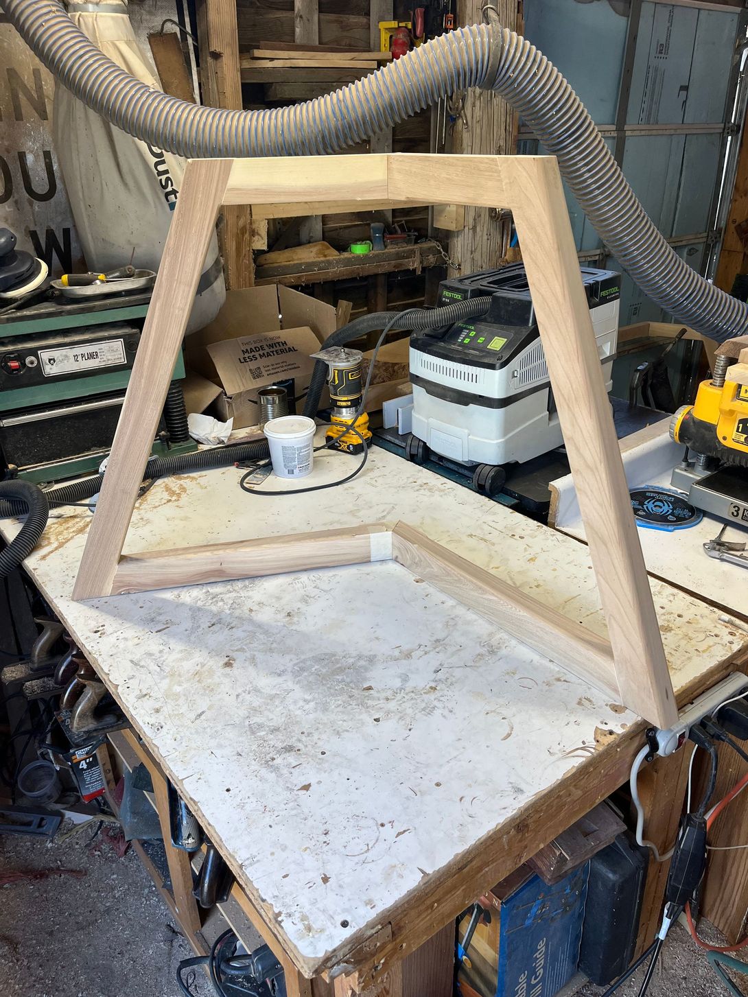 Wooden table frame in a workshop, angled legs, connected to the tabletop.
