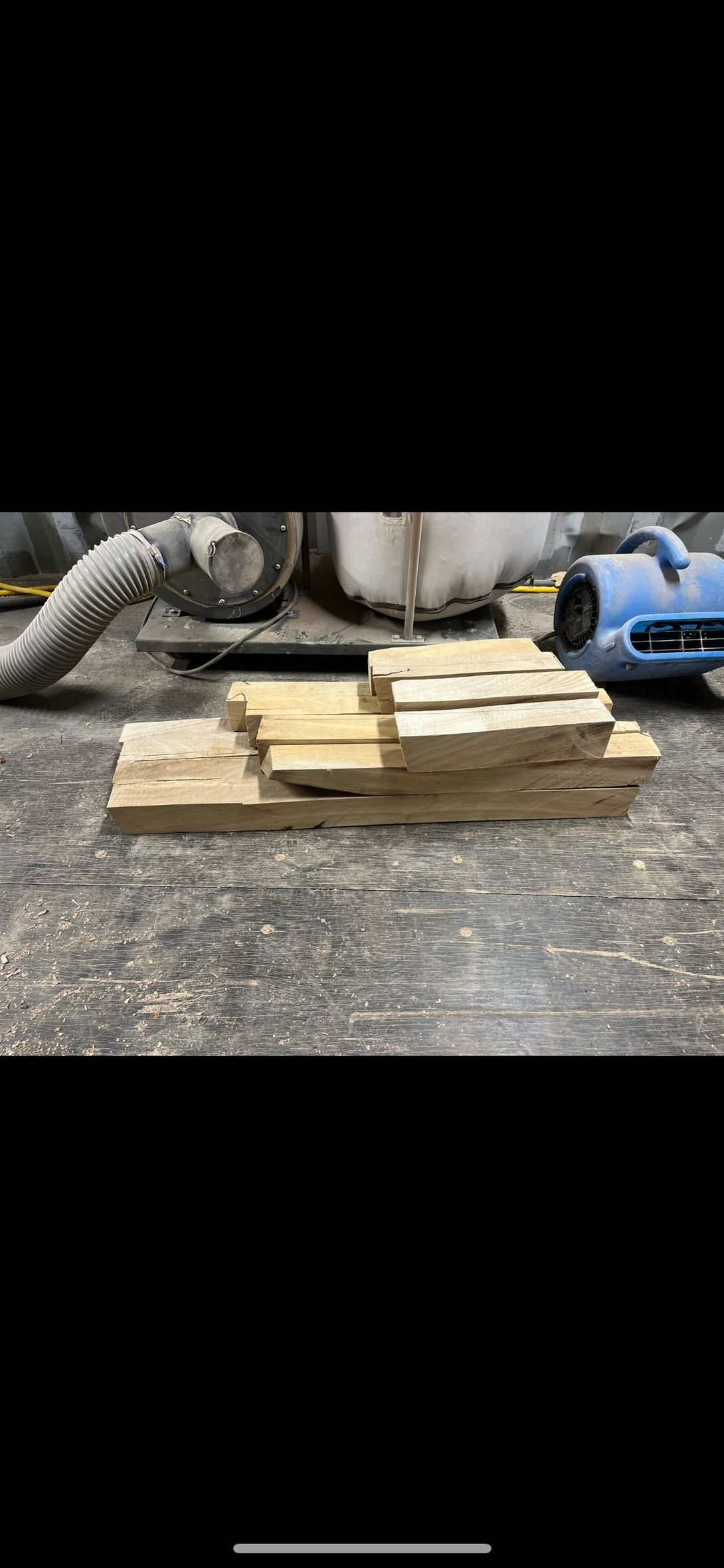 Wooden planks stacked on a workbench, with a tool and machine visible in the background.