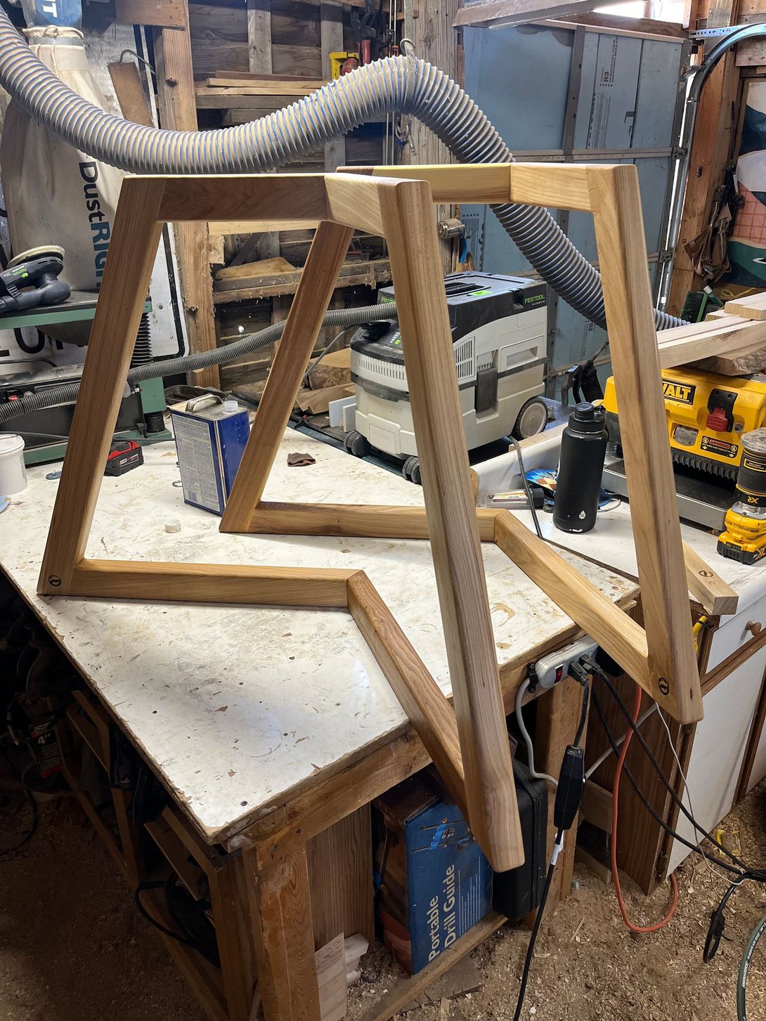 Two wooden table frames, unfinished, on a cluttered workbench in a workshop.