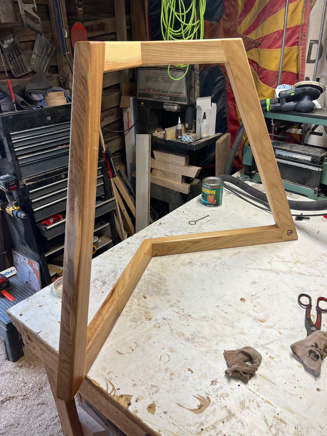 Wooden frame, partially assembled, on a workbench in a workshop, with tools visible.