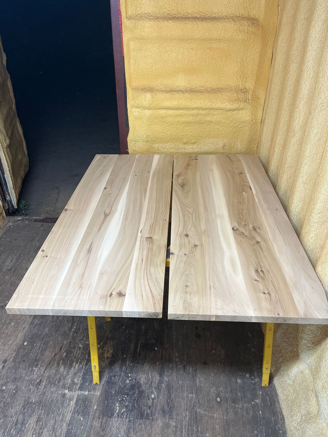 Two light wooden table tops on yellow supports in a dimly lit room.