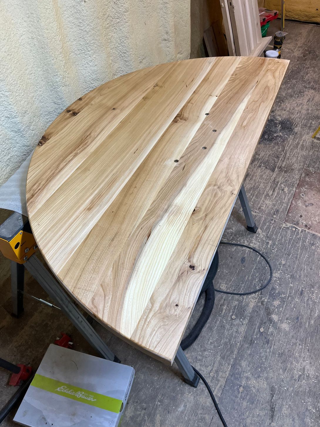 Half-circle wooden table in a workshop setting, light brown wood grain, resting on sawhorses.