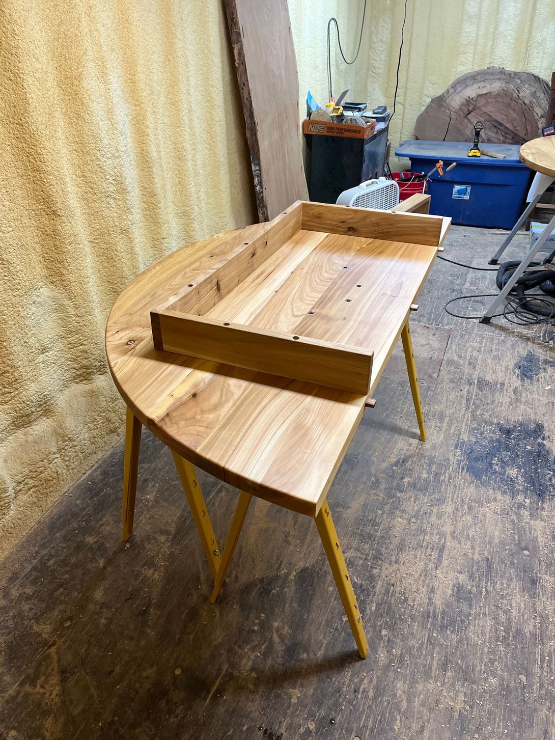 Wooden half-circle table with yellow legs, a wooden tray, in a workshop.