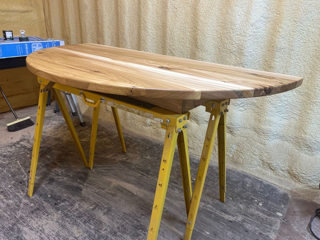 Wooden table top on yellow sawhorses in a workshop setting.