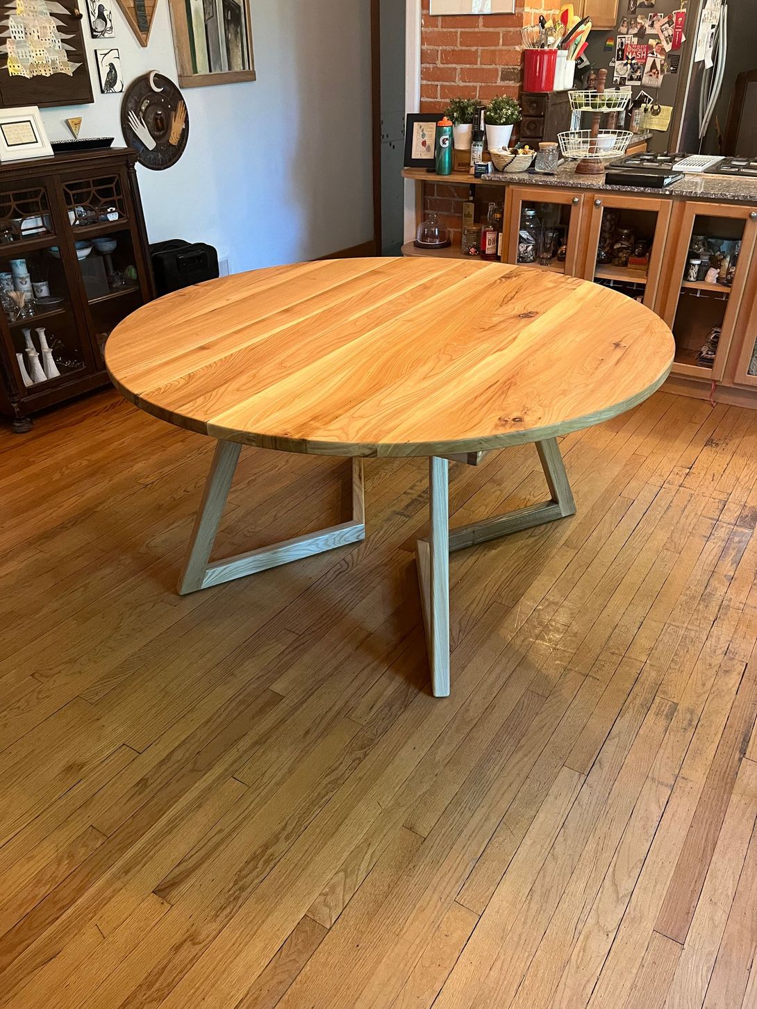 Round wooden dining table with light wood top and metal legs in a home interior.