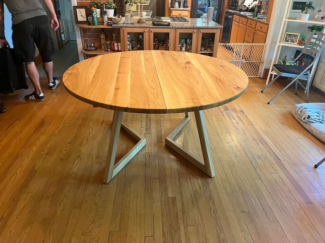 Round wooden dining table with angled legs in a room with hardwood floors.