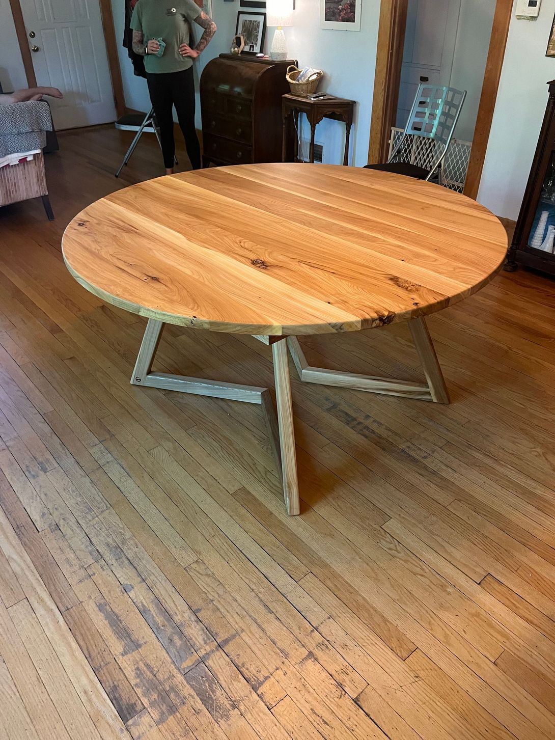 Round wooden dining table with cross-legged base in a room with hardwood floors.