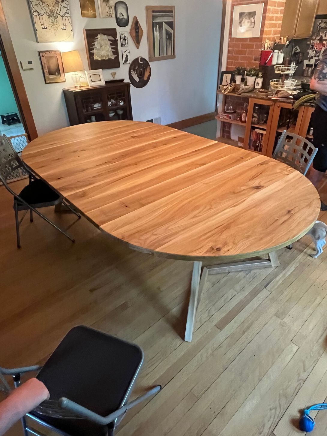 Oval wooden dining table in a room with various pictures on the wall.