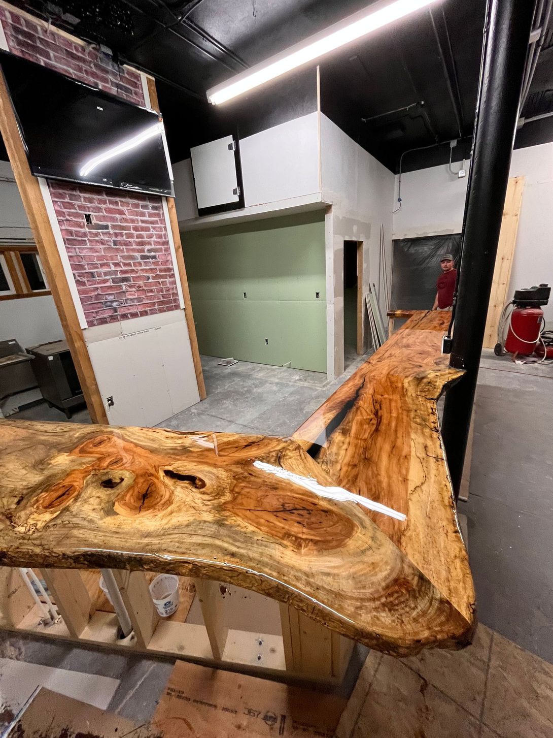 Live-edge wood bar in a space under construction, with a brick wall and unfinished walls in the background.