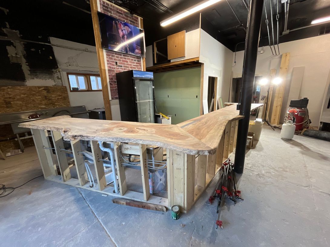 Bar under construction in a commercial space; wooden frame with unfinished counter, exposed wall, and dim lighting.