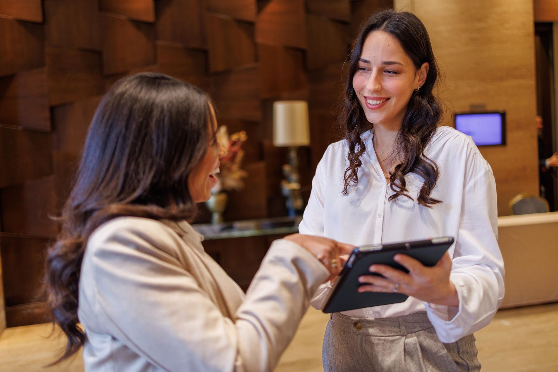 Foto da recepção de um hotel moderno com tablets para check‑in on‑line e equipe atendendo hóspedes