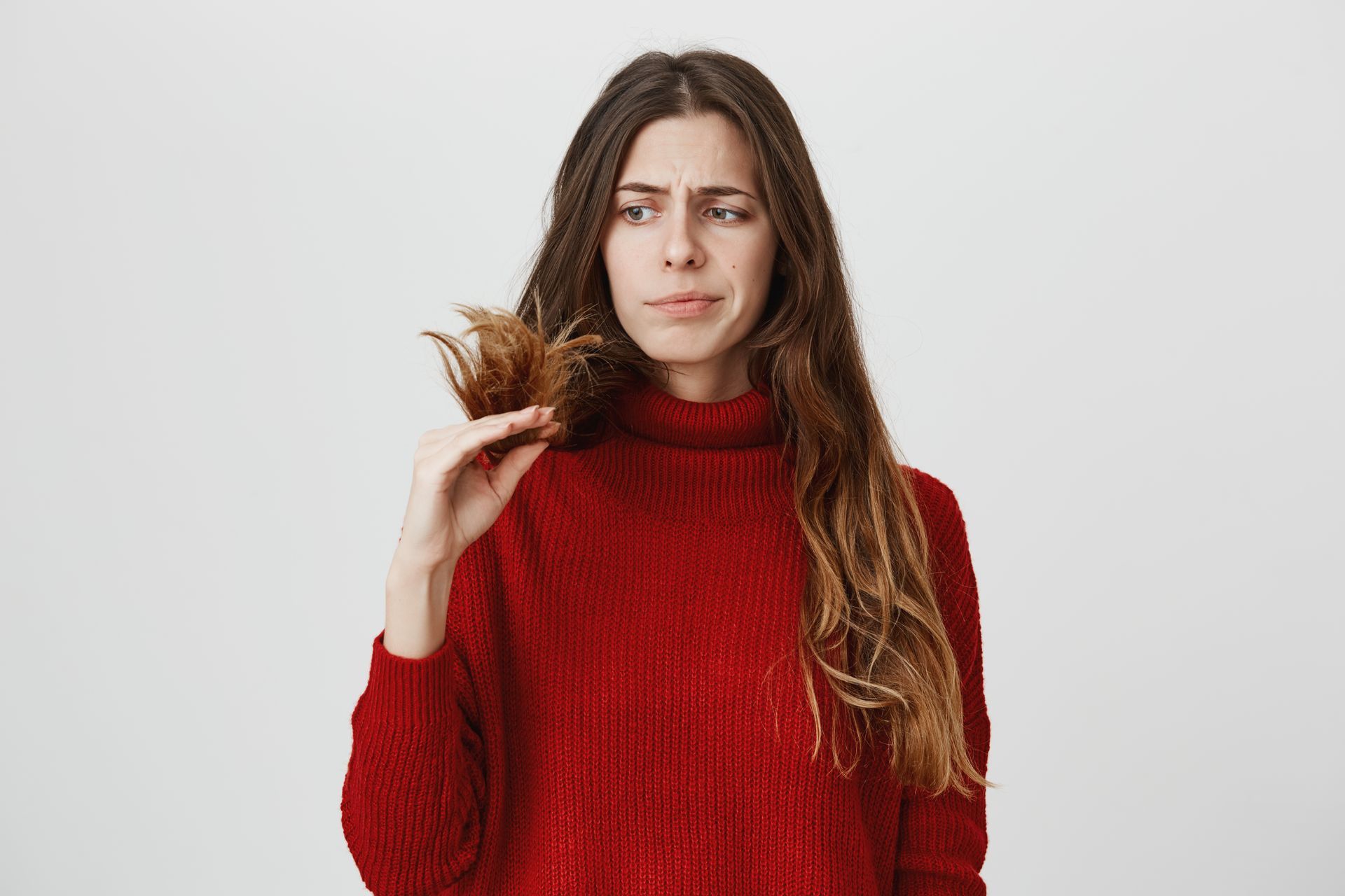 a woman in a red sweater is holding a piece of her hair .
