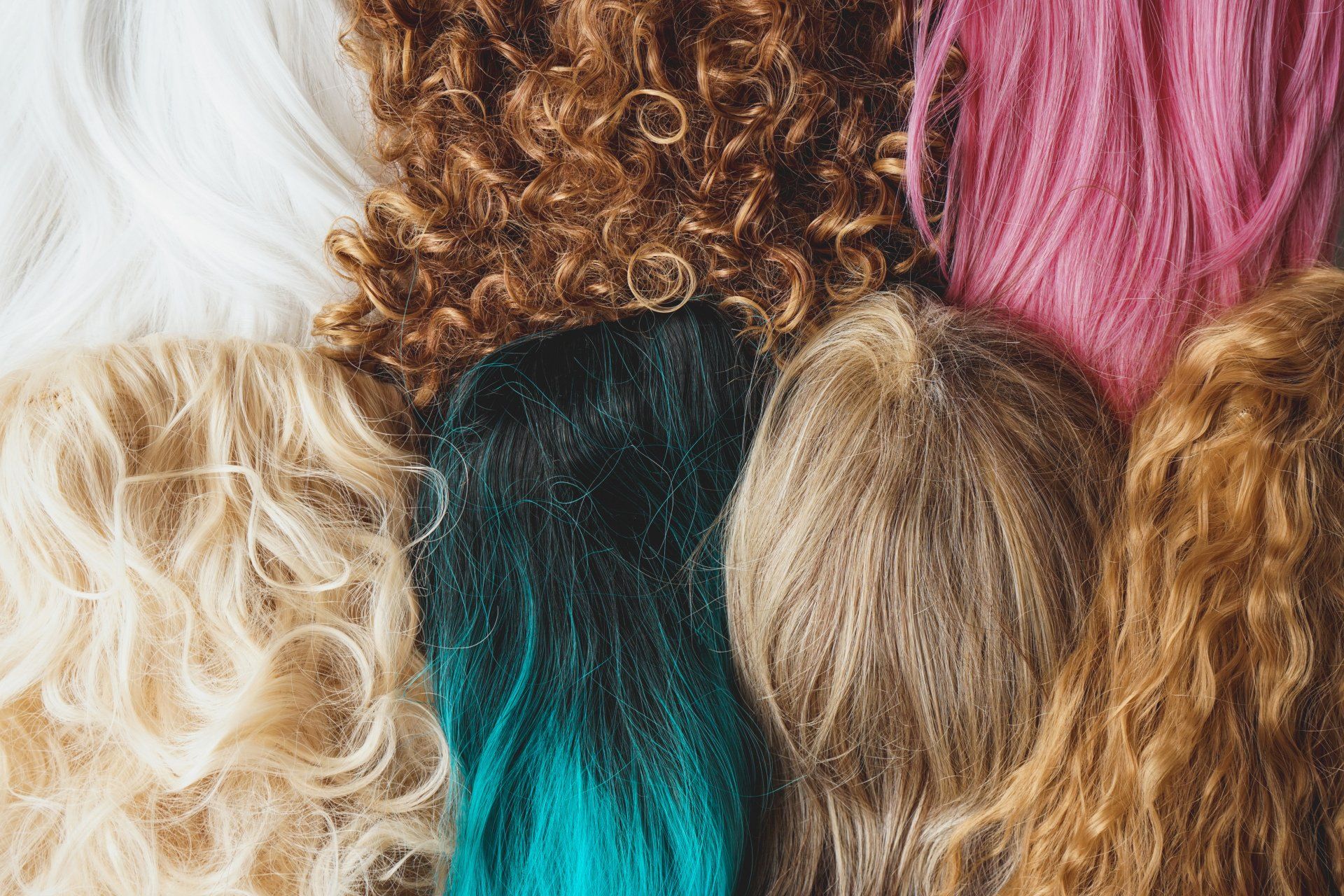 a group of wigs of different colors lies on top of each other on the table.