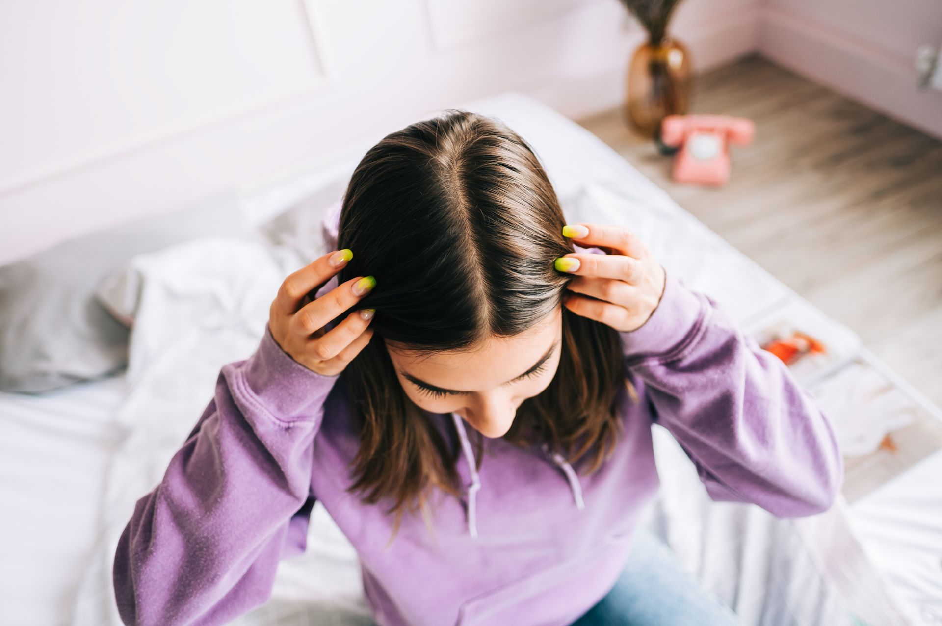 a woman in a purple sweatshirt is sitting on a bed holding her hair .