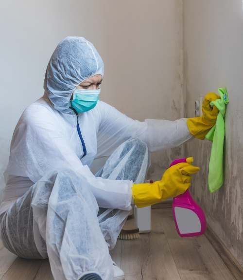 A person in a protective suit and mask is cleaning a wall.