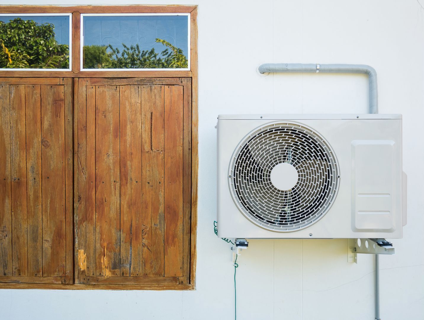 A white air conditioner is mounted on a white wall next to a wooden window.