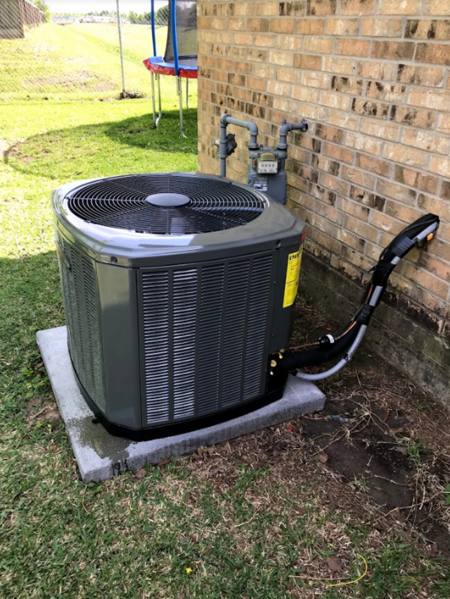A large air conditioner is sitting on top of a concrete slab next to a brick wall.