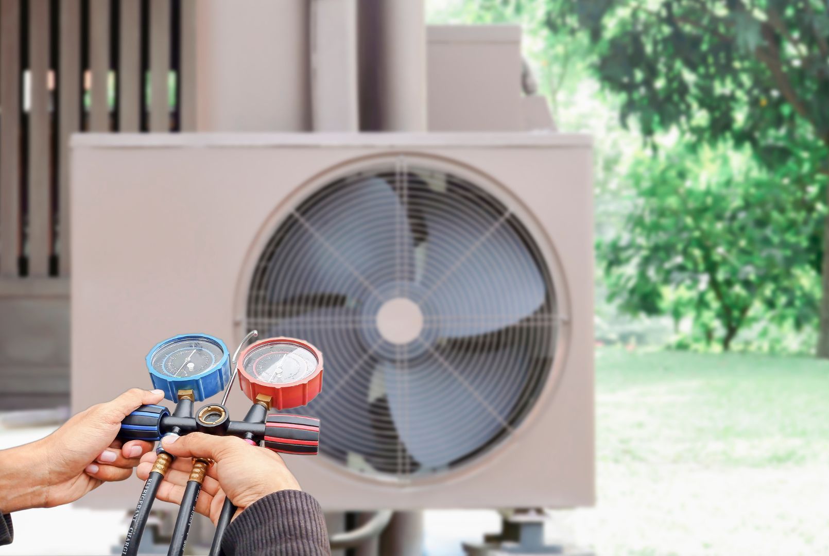 A person is holding a pair of gauges in front of an air conditioner.