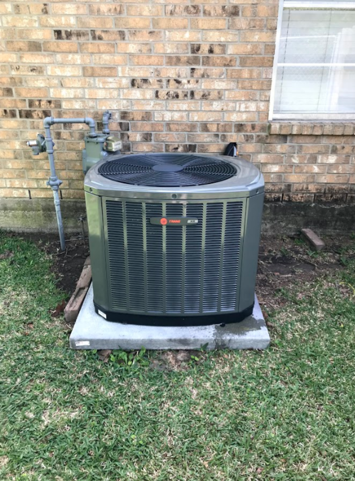 An air conditioner is sitting on top of a concrete platform in front of a brick building.