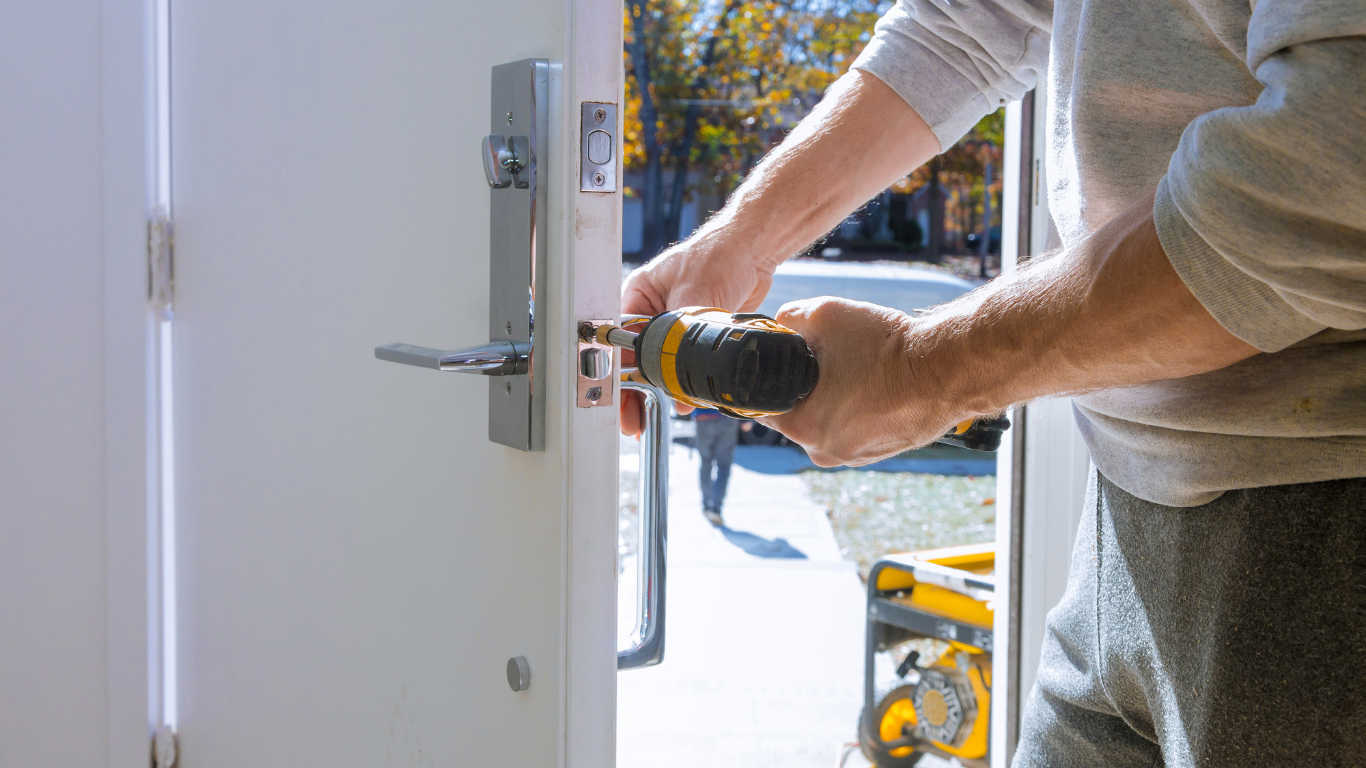 A person installing a door lock with a drill outdoors.