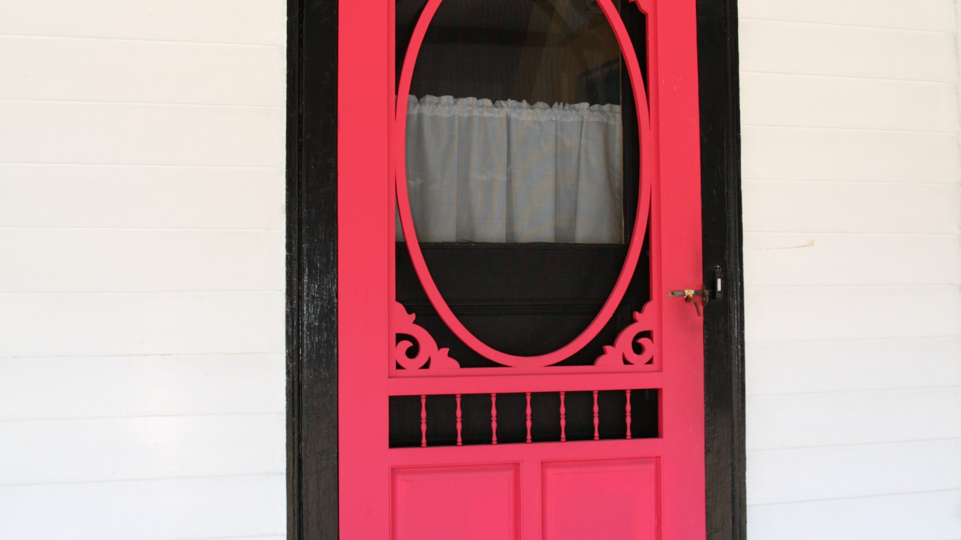 Bright pink screen door with black trim, a decorative oval window, and a white curtain.