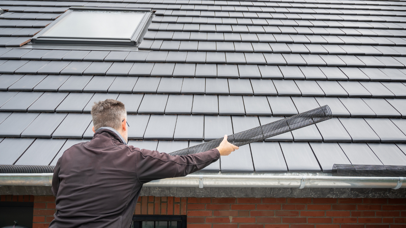 Man installs gutter guard on roof above brick wall.