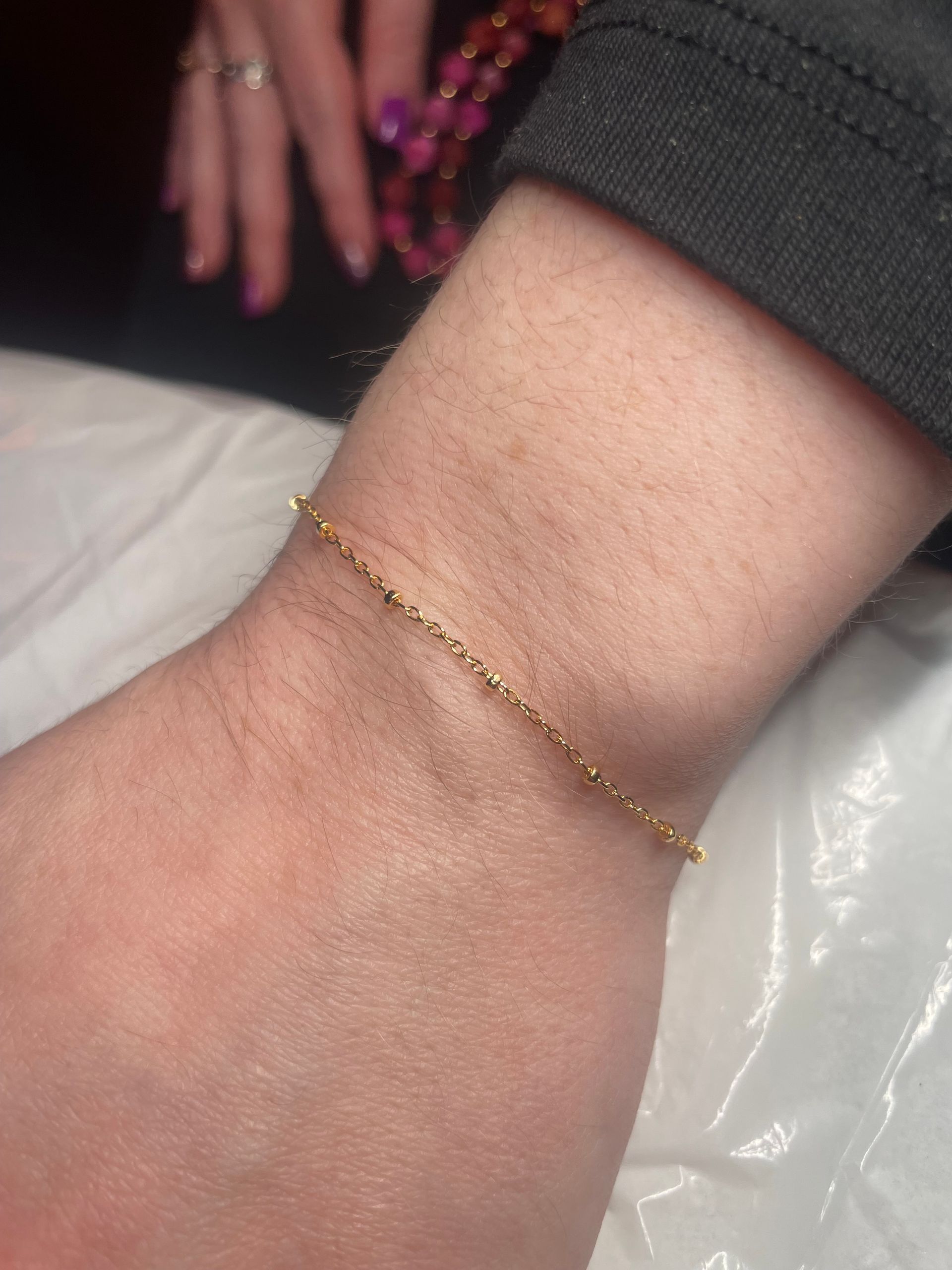 A person wearing a gold bracelet on their wrist