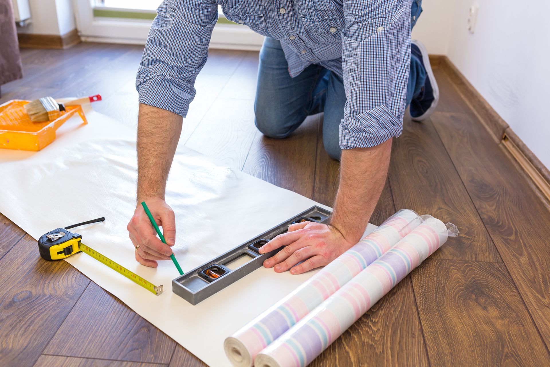 A man is measuring a roll of wallpaper with a level.